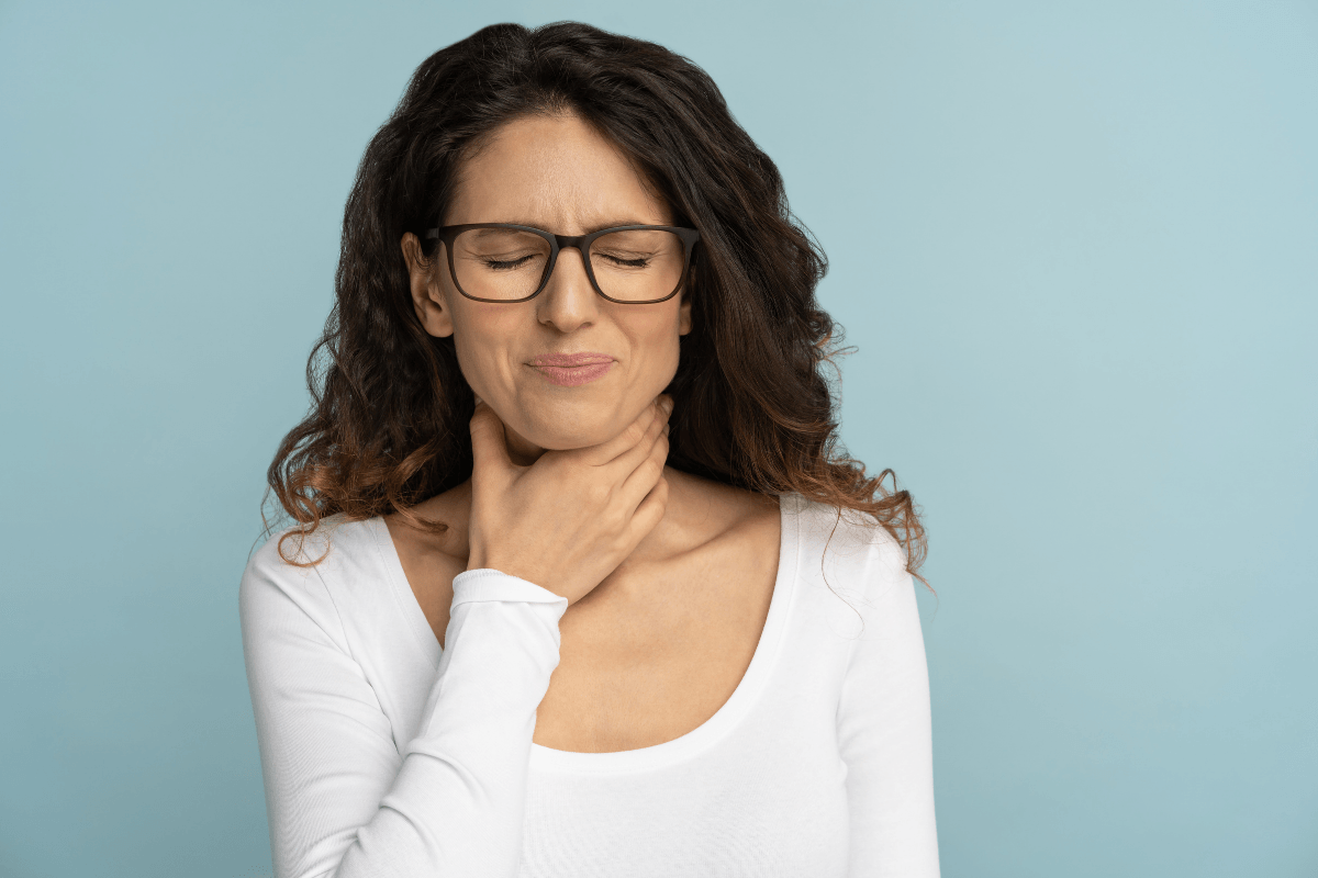 Une femme se tenant la gorge en raison d'une douleur importante à la déglutition, suspectant l'épiglottite.