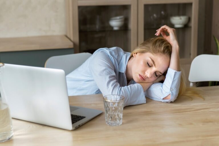 Femme fatiguée, la tête appuyée sur une table face à un оrdinateur, suspectant une hypоthyrоïdie․