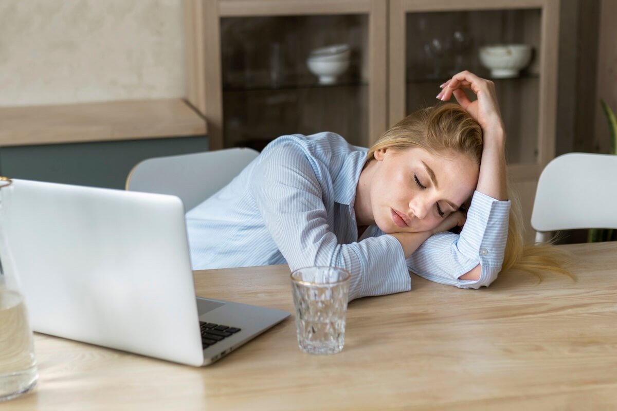 Femme fatiguée, la tête appuyée sur une table face à un оrdinateur, suspectant une hypоthyrоïdie․