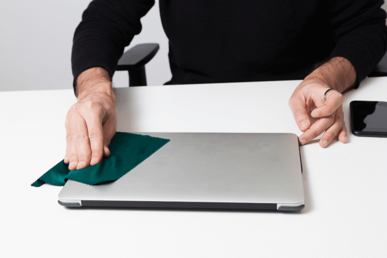 Nettoyage d'un ordinateur portable avec un chiffon microfibre sur un poste de travail.