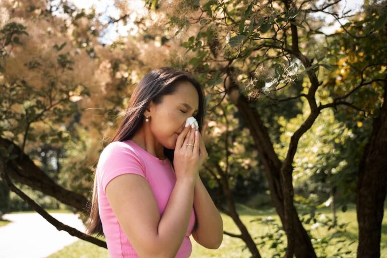 Une femme se mouchant en extérieur suspectant les symptômes de rhume en été.