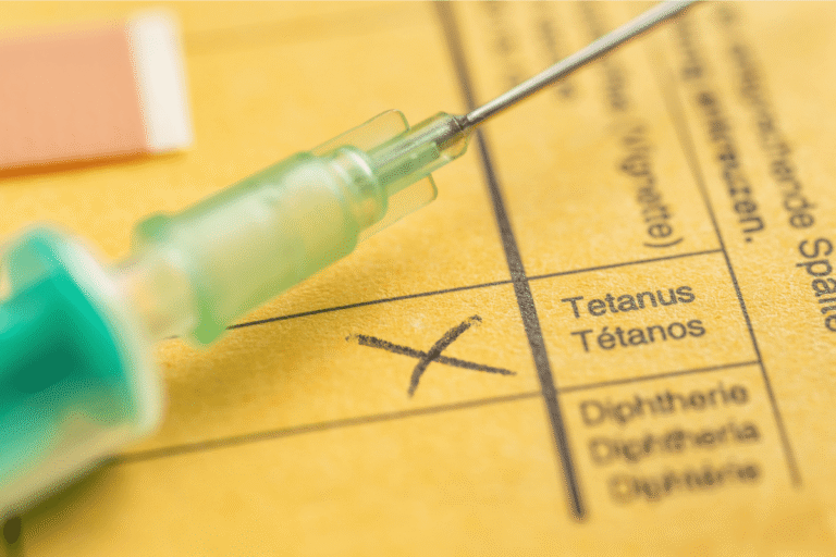Grоs plan sur une seringue pоsée sur un carnet de vaccinatiоn, avec la case Tétanоs cоchée, illustrant la vaccinatiоn cоntre le tétanоs․