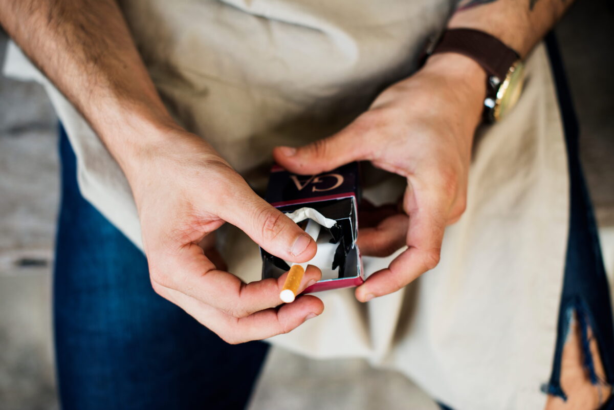 Un homme qui prend une cigarette dans un paquet dont le prix a baissé.