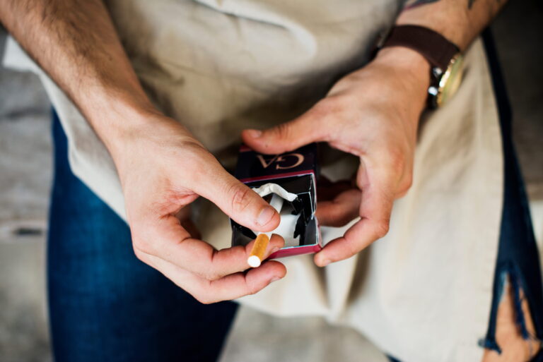 Un homme qui prend une cigarette dans un paquet dont le prix a baissé.