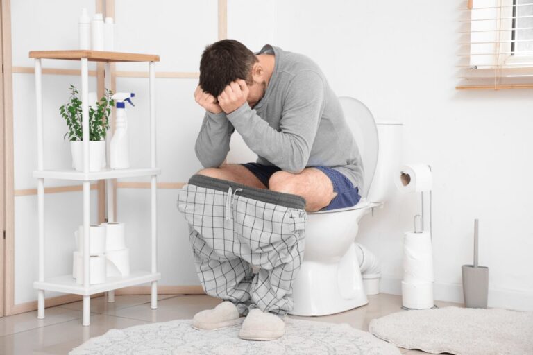 Homme assis sur des toilettes, le pantalon baissé, la tête penchée et les mains posées sur le front.