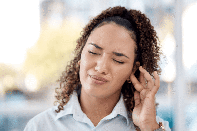 Femme ferme les yeux en portant sa main près de l'oreille, affichant une expression gênée, suspectant la avoir un acouphène pulsatile․
