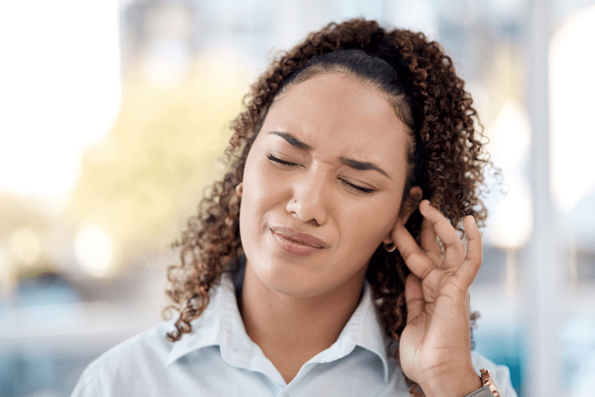 Femme ferme les yeux en portant sa main près de l'oreille, affichant une expression gênée, suspectant la avoir un acouphène pulsatile․