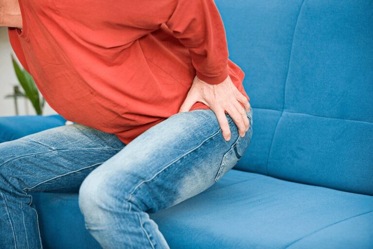 Homme assis sur un canapé se tenant le côté de la hanche en raison d’une douleur, suspectant la bursite trochantérienne.