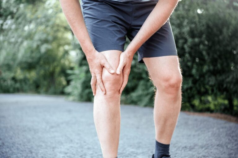 Homme debout se tenant le genou douloureux après un traumatisme, suspectant une fracture de la rotule.