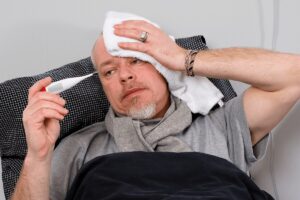 Personne alitée avec un thermomètre et une serviette sur le front en raison d’une forte fièvre.