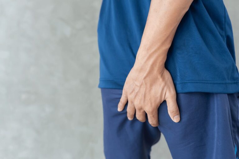 Personne posant sa main sur la partie supérieure de la fesse, près du coccyx, en raison d’une gêne, suspectant un sinus pilonidal.