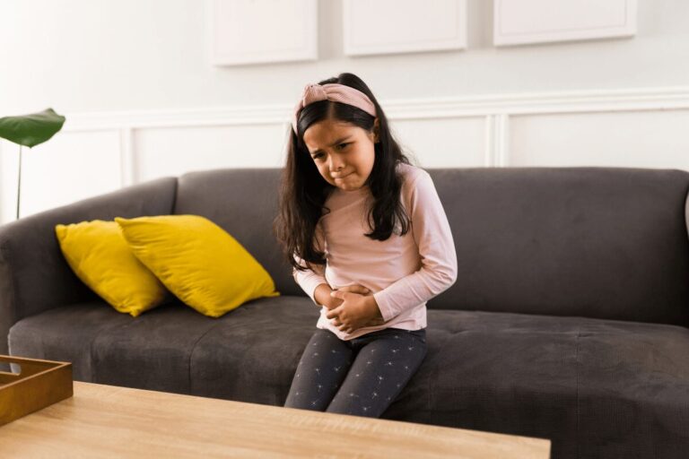 Jeune fille assise sur un canapé, les mains posées sur le ventre avec une expression douloureuse, suspectant un oxyures.