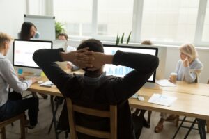 Un homme en plein burn-out, incapable de se concentrer sur son travail, reste assis, les bras croisés derrière la tête, en signe d’épuisement.