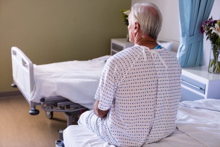 Un homme âgé, hospitalisé pour un cancer de la prostate, est assis au bord de son lit.