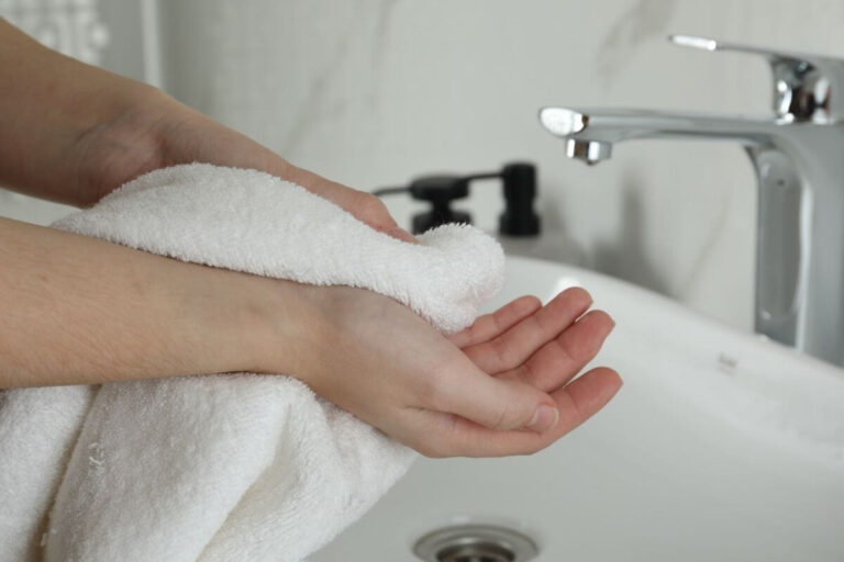 Personne se séchant délicatement les bras avec une serviette, suspectant des démangeaisons après la douche.