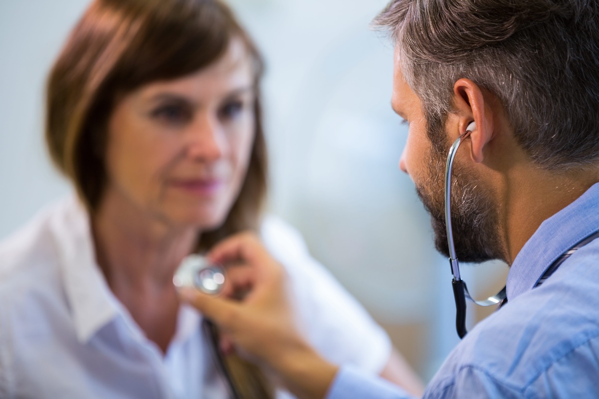 Un médecin généraliste, stéthoscope aux oreilles, ausculte une patiente lors d’une consultation dans son cabinet médical.