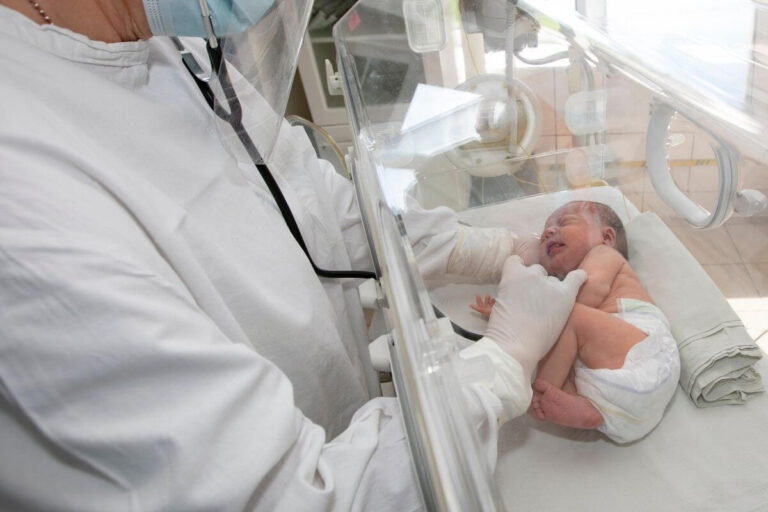 Un professionnel de santé examine un nouveau-né installé dans une couveuse à l’hôpital.