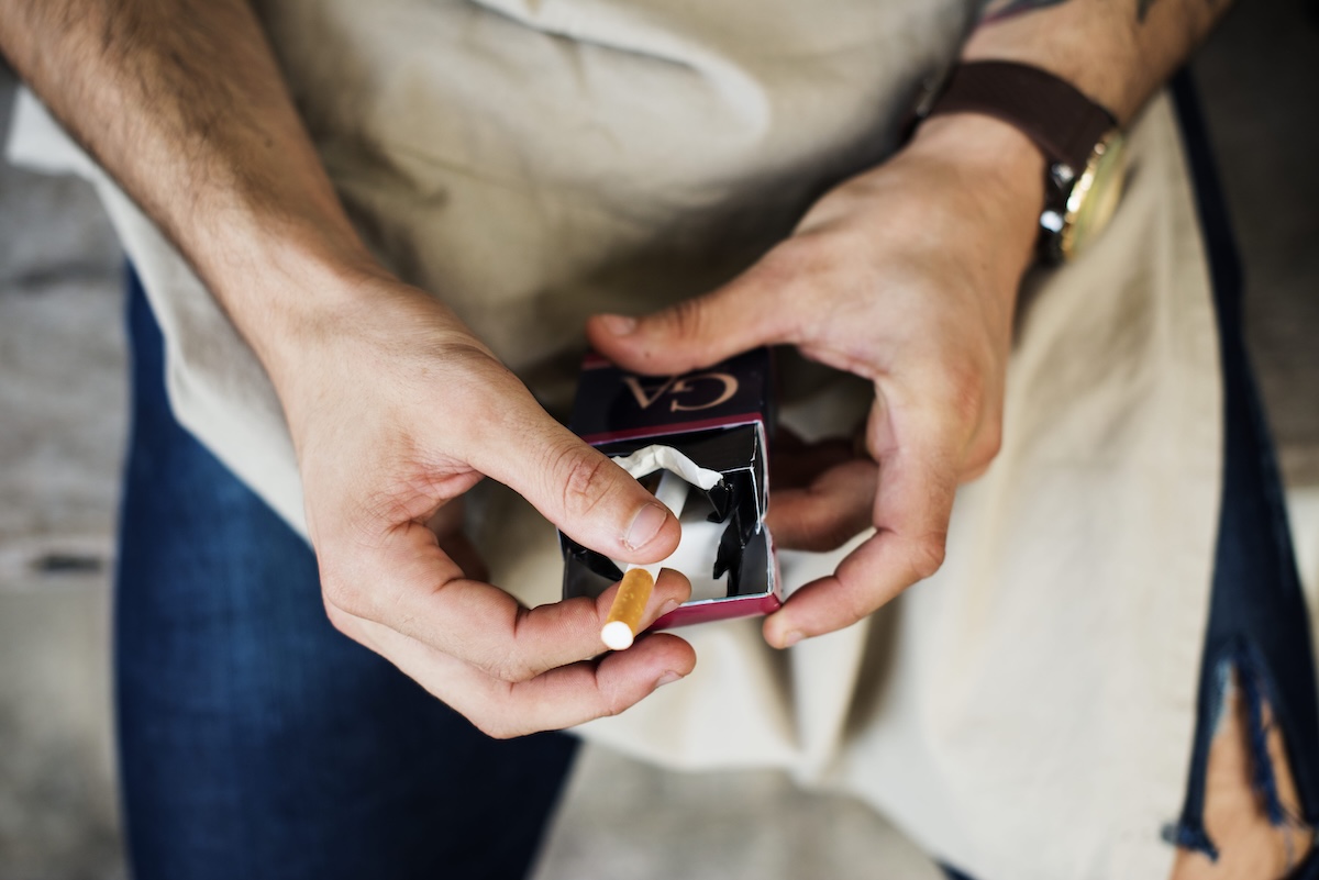 Un homme qui prend une cigarette dans son paquet.