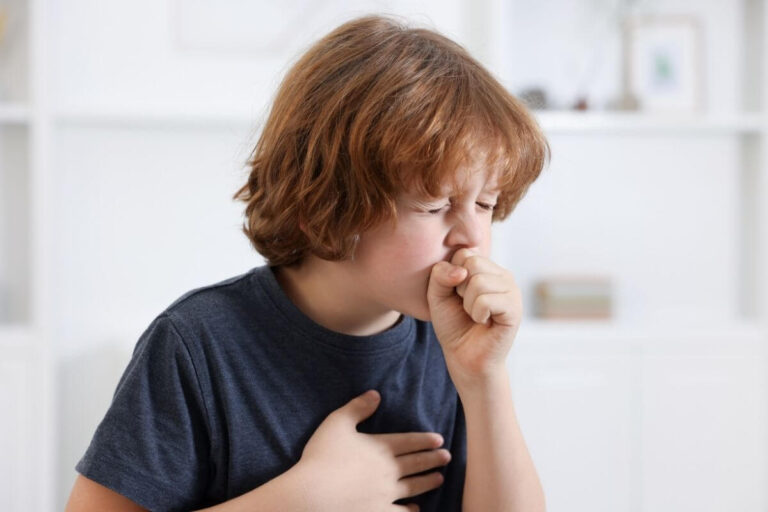Un enfant tousse dans son poing, une main posée sur la poitrine, pour illustrer la toux persistante pouvant être associée à une infection par Mycoplasma pneumoniae.