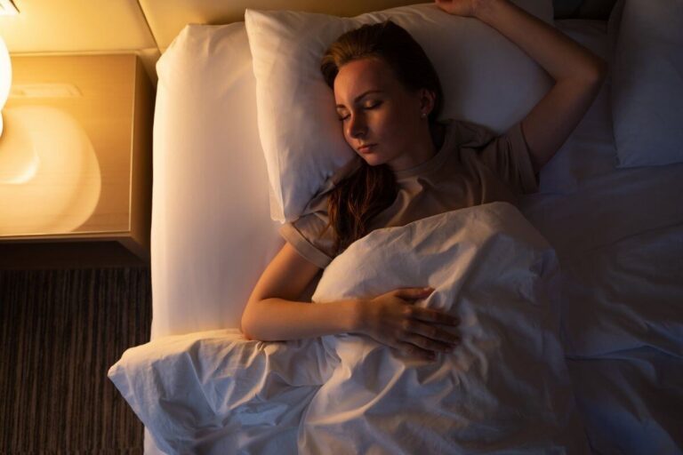 Une femme dort dans son lit, une lampe de chevet allumée près de son visage, ce qui perturbe son horloge biologique․
