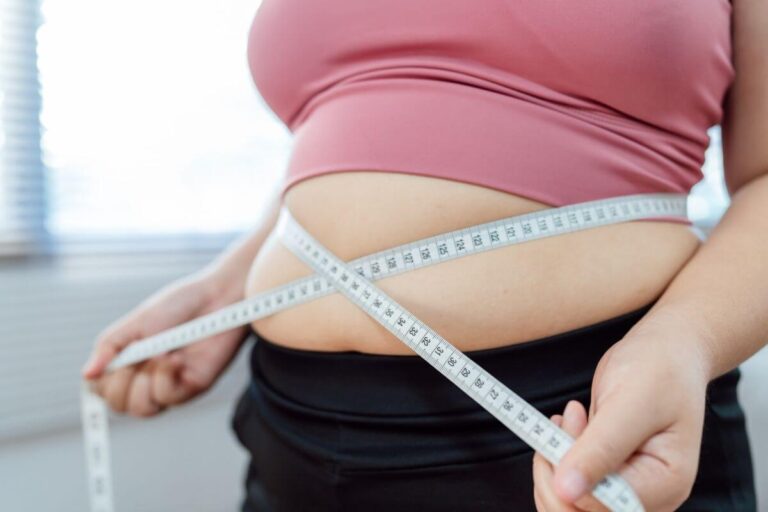 Une personne mesure son tour de taille à l’aide d’un mètre ruban placé autour de son abdomen.