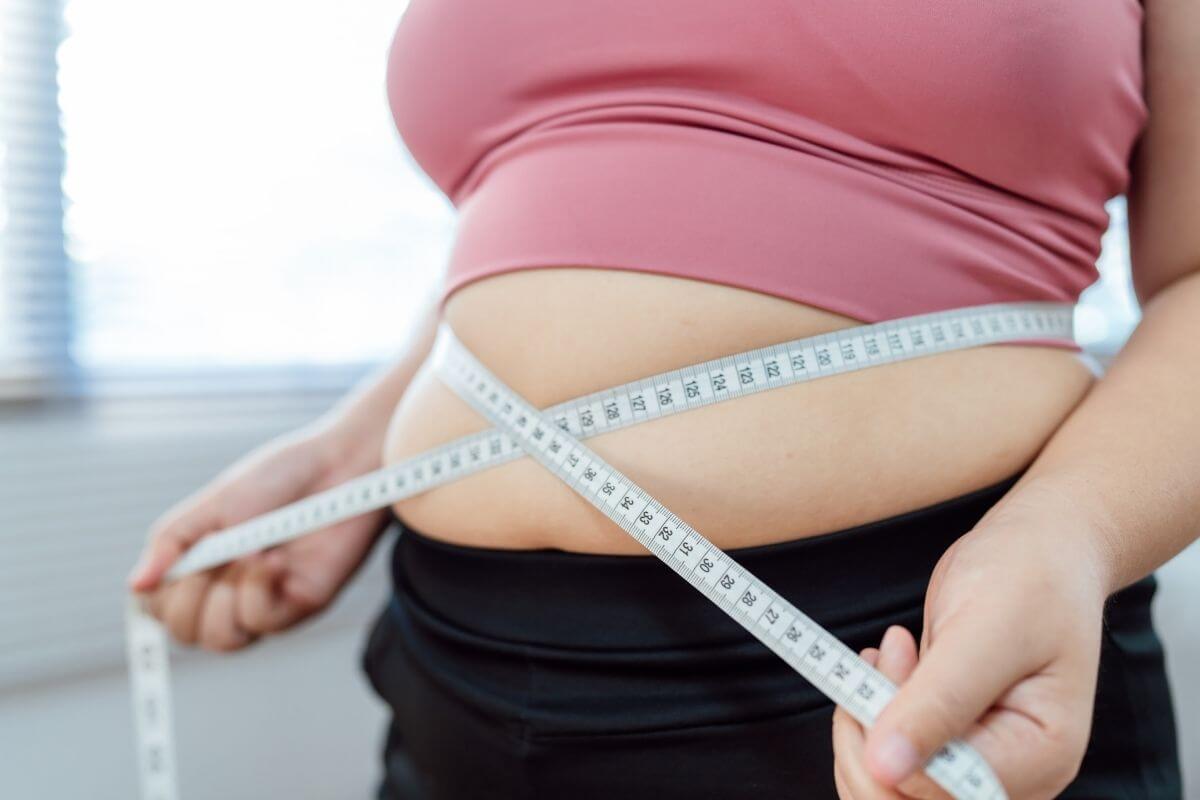 Une personne mesure son tour de taille à l’aide d’un mètre ruban placé autour de son abdomen.