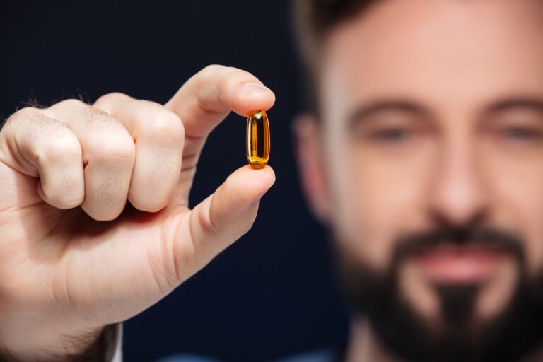 Un homme tient entre son pouce et son index une capsule de vitamine D.