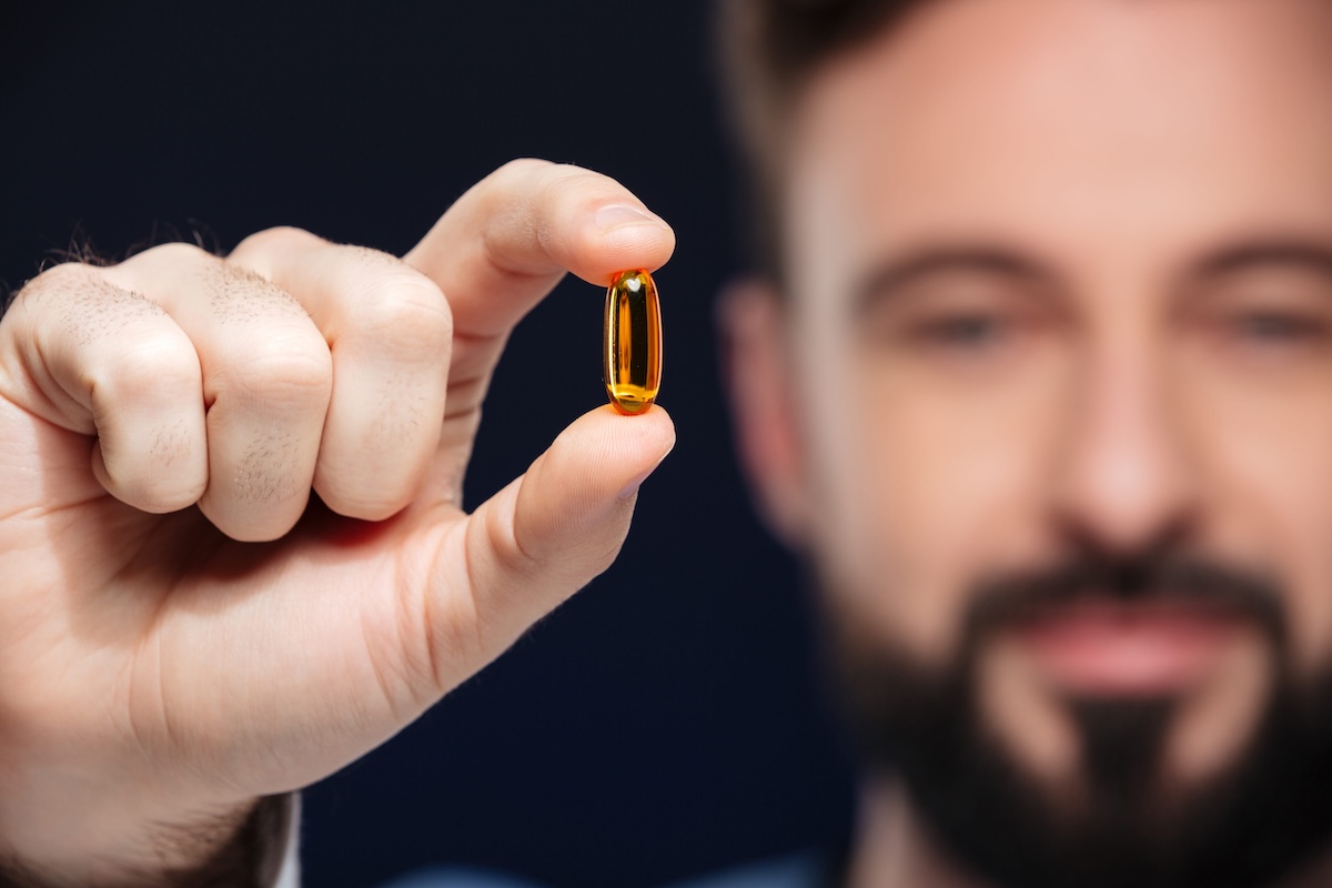 Un homme tient entre son pouce et son index une capsule de vitamine D.