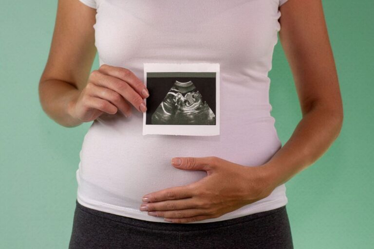 Une femme enceinte tient une image d’échographie devant son ventre tout en posant une main sur celui-ci.