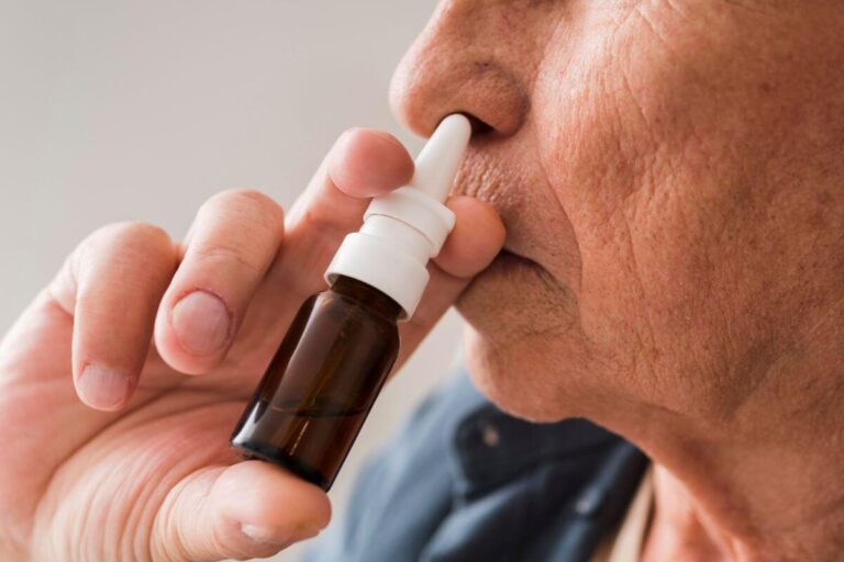 Un homme introduit l’embout d’un flacon pulvérisateur dans une narine pour utiliser un spray nasal.