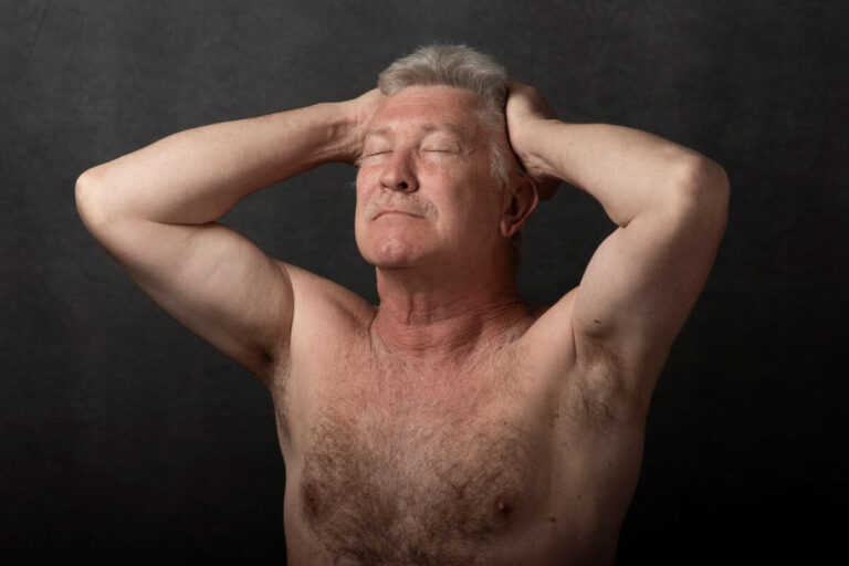 Un homme âgé torse nu garde les yeux fermés et pose ses deux mains derrière sa tête.